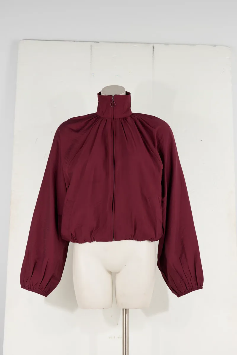 A burgundy zip jacket with a gathered high neck and balloon sleeves on a headless bust